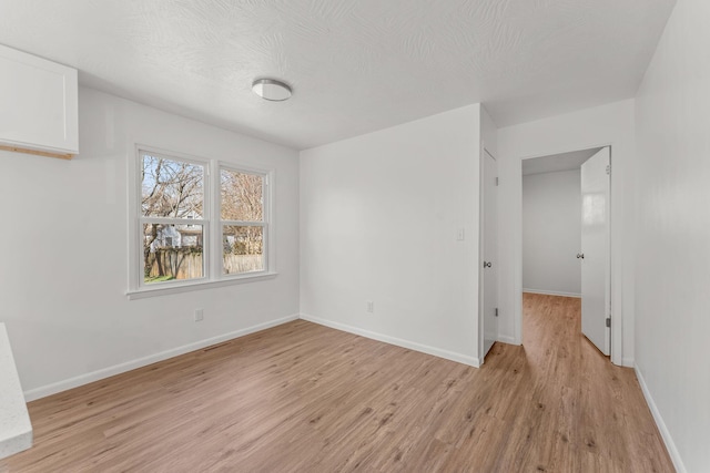 empty room featuring light wood-style floors, baseboards, and a textured ceiling