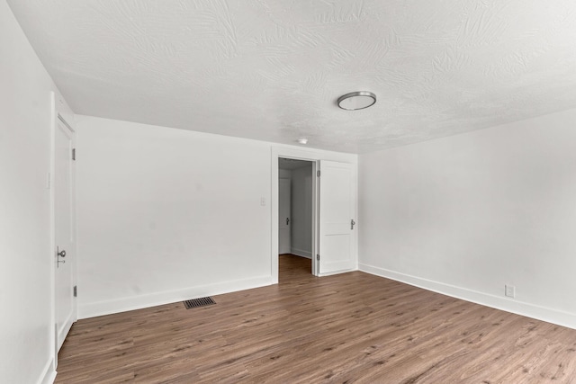 empty room with visible vents, wood finished floors, baseboards, and a textured ceiling