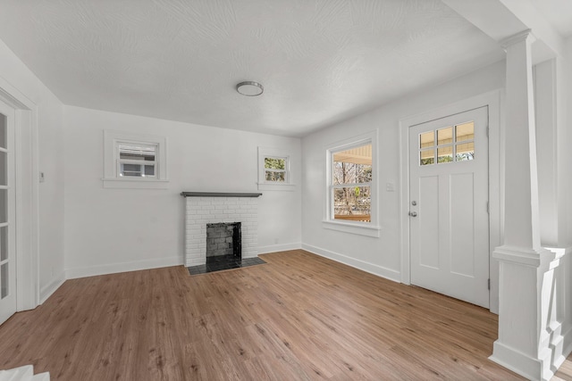 unfurnished living room featuring decorative columns, baseboards, a brick fireplace, and light wood-style flooring