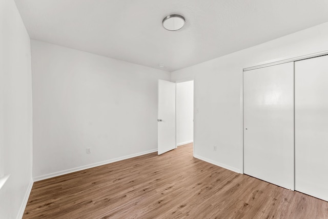 unfurnished bedroom with wood finished floors, baseboards, and a closet