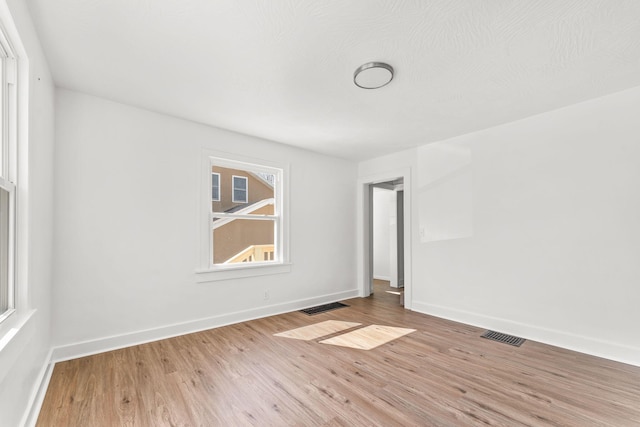 spare room featuring wood finished floors, visible vents, and baseboards