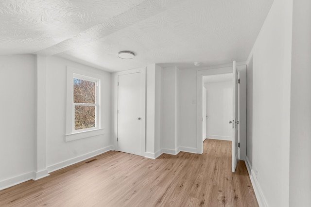 unfurnished bedroom with visible vents, a textured ceiling, a closet, light wood finished floors, and baseboards