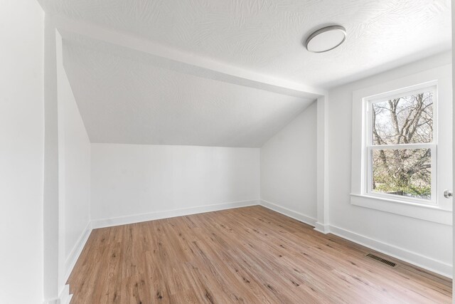 additional living space featuring visible vents, a textured ceiling, and light wood-style floors