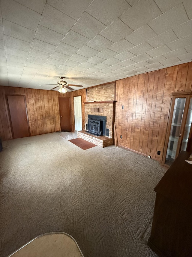 unfurnished living room with carpet floors, wooden walls, a brick fireplace, and ceiling fan