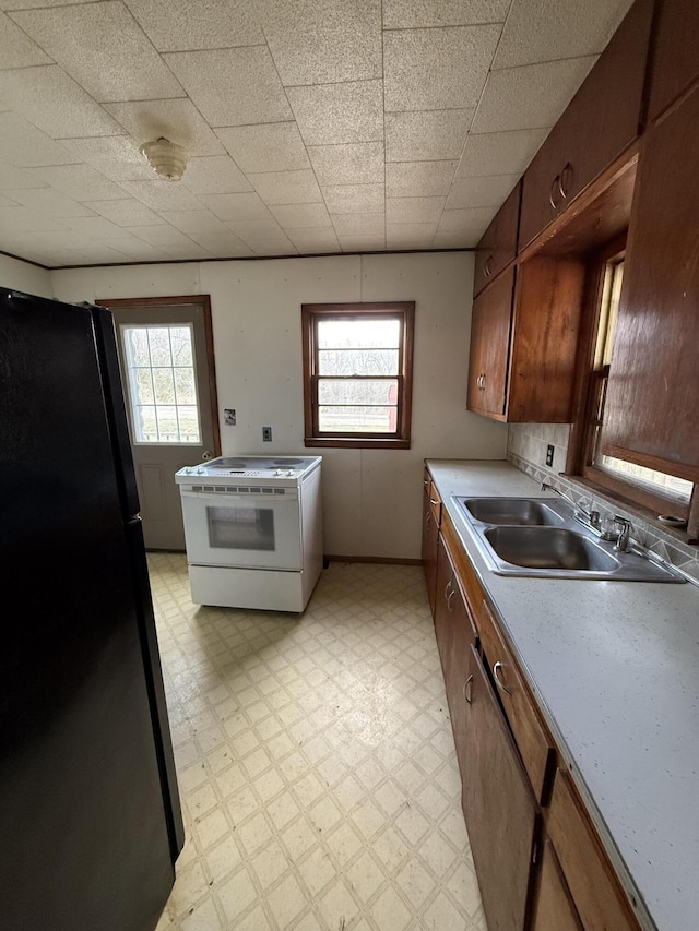 kitchen featuring light floors, freestanding refrigerator, a sink, light countertops, and white range with electric stovetop