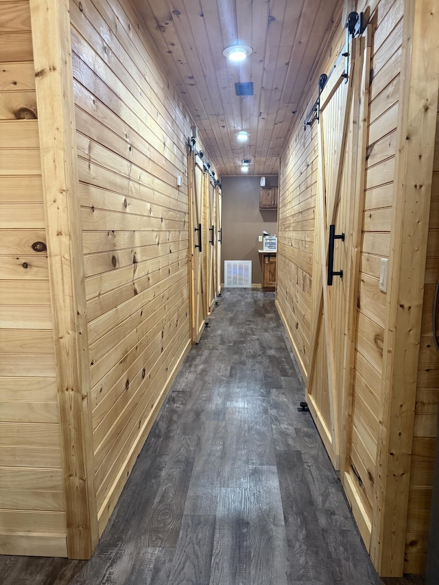 hallway with wood ceiling, a barn door, visible vents, and wood walls