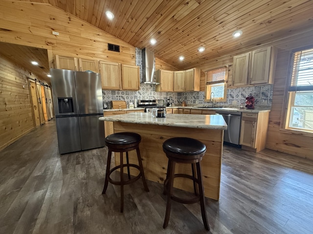 kitchen featuring a sink, stainless steel appliances, wall chimney exhaust hood, wood walls, and vaulted ceiling