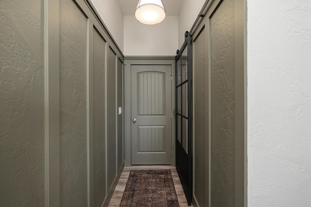 corridor with a barn door, dark wood-style flooring, and a textured wall