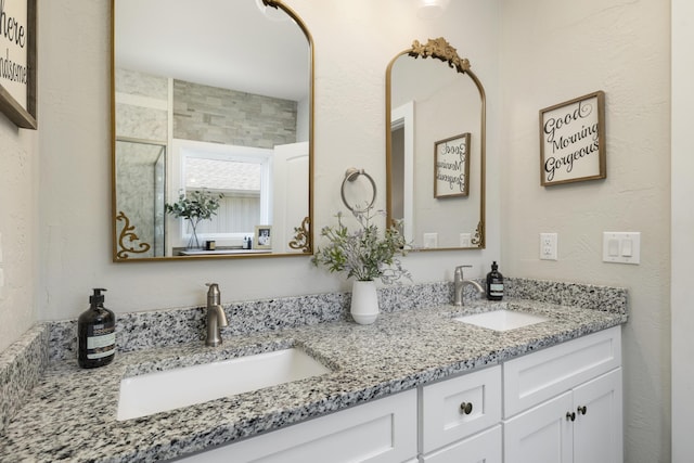 full bathroom with double vanity, a stall shower, a textured wall, and a sink