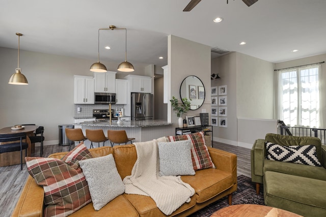 living room with light wood-type flooring, visible vents, a ceiling fan, recessed lighting, and baseboards