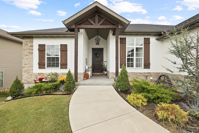 entrance to property featuring stone siding, a shingled roof, and a yard