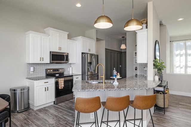 kitchen featuring wood finished floors, light stone countertops, a breakfast bar, a peninsula, and stainless steel appliances