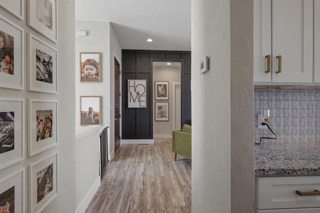 corridor featuring recessed lighting, light wood-style flooring, baseboards, and a textured wall