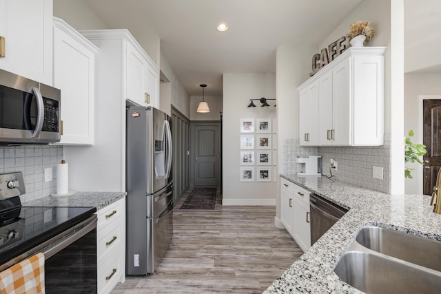 kitchen with light stone countertops, light wood-style flooring, a sink, appliances with stainless steel finishes, and white cabinetry