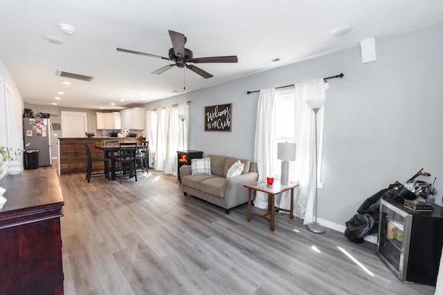 living area featuring baseboards, light wood-style floors, visible vents, and ceiling fan