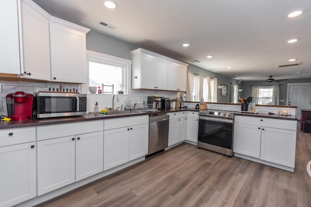 kitchen featuring visible vents, a peninsula, a sink, stainless steel appliances, and dark countertops