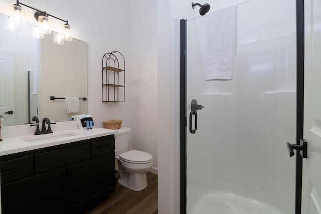 bathroom featuring wood finished floors, toilet, a stall shower, and vanity