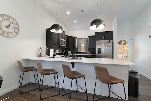 kitchen featuring light countertops, a kitchen bar, appliances with stainless steel finishes, a peninsula, and dark wood-style flooring