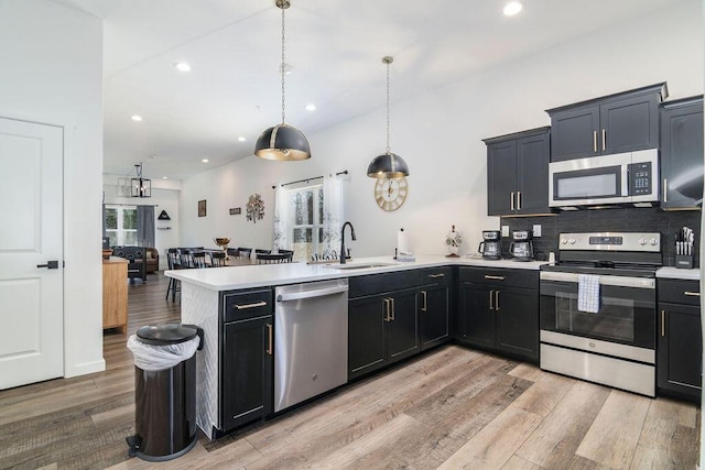 kitchen featuring light wood finished floors, light countertops, appliances with stainless steel finishes, a peninsula, and a sink