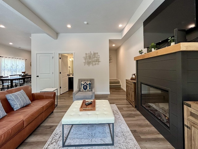 living area with a glass covered fireplace, baseboards, wood finished floors, and recessed lighting