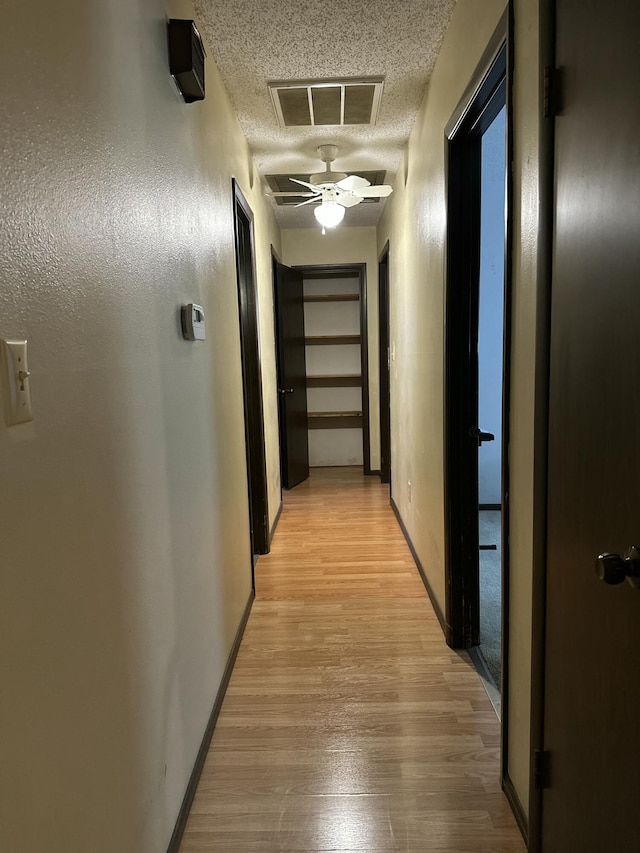 hall featuring light wood-style flooring, baseboards, visible vents, and a textured ceiling