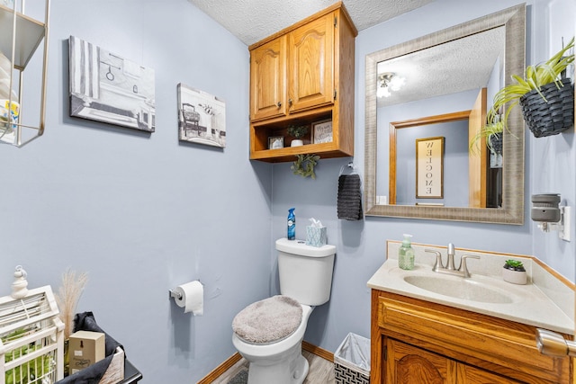 bathroom with baseboards, a textured ceiling, vanity, and toilet