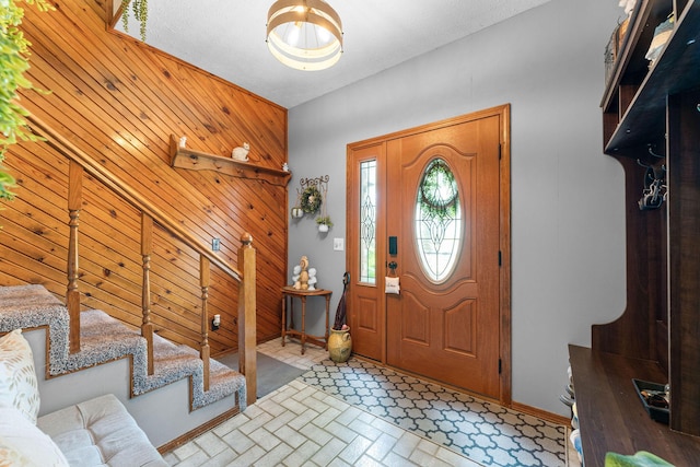 foyer entrance featuring brick floor, stairway, baseboards, and wood walls