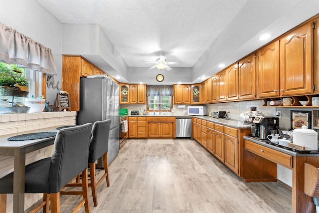 kitchen with a ceiling fan, a textured ceiling, stainless steel appliances, brown cabinetry, and light wood finished floors