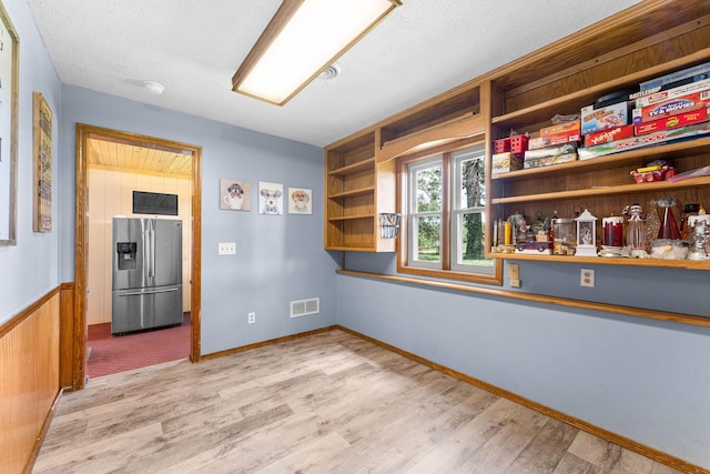 spare room featuring visible vents, wainscoting, a textured ceiling, and light wood-style floors