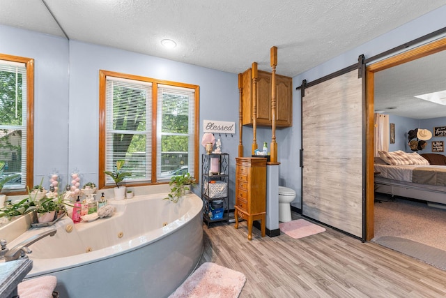 ensuite bathroom featuring toilet, a textured ceiling, wood finished floors, ensuite bath, and a tub with jets