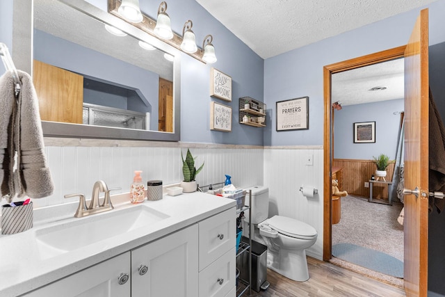 bathroom featuring toilet, vanity, wainscoting, wood finished floors, and a textured ceiling