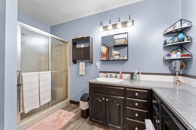 full bath with vanity, wood finished floors, a stall shower, and a textured ceiling