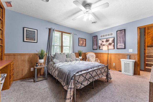 bedroom with a textured ceiling, wood walls, wainscoting, and carpet