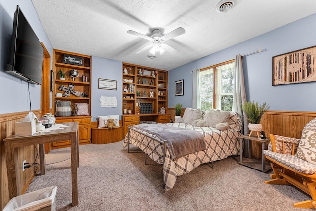 bedroom featuring visible vents, ceiling fan, light carpet, wainscoting, and a textured ceiling