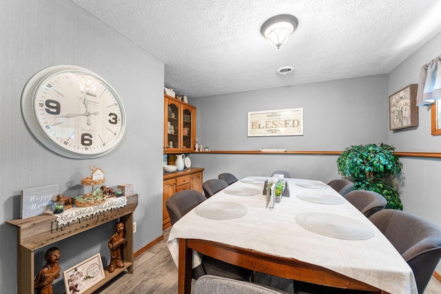 dining area with visible vents, light wood-style flooring, and a textured ceiling