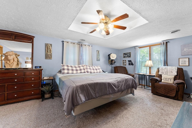 bedroom featuring visible vents, a tray ceiling, carpet floors, a textured ceiling, and a ceiling fan