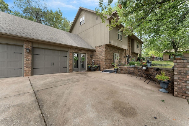 exterior space with brick siding, a shingled roof, concrete driveway, french doors, and a garage