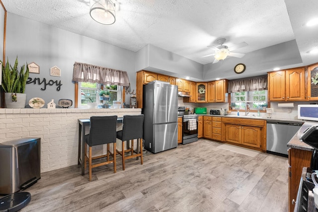 kitchen with a sink, stainless steel appliances, light wood-style floors, brown cabinetry, and ceiling fan