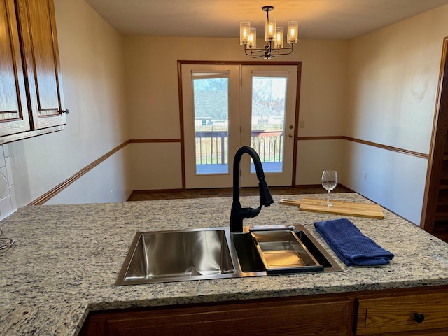 kitchen with an inviting chandelier, pendant lighting, light stone counters, and a sink