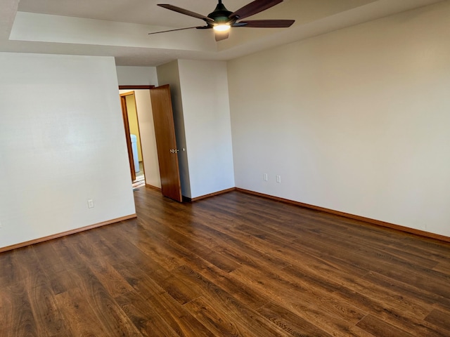 spare room featuring a raised ceiling, baseboards, dark wood-type flooring, and ceiling fan