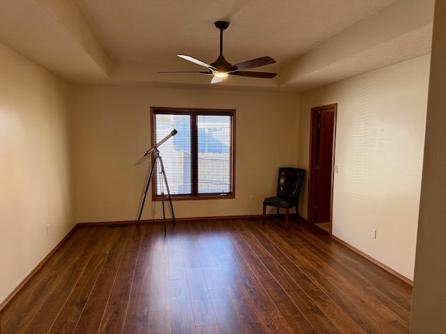 empty room featuring ceiling fan, a tray ceiling, and dark wood finished floors