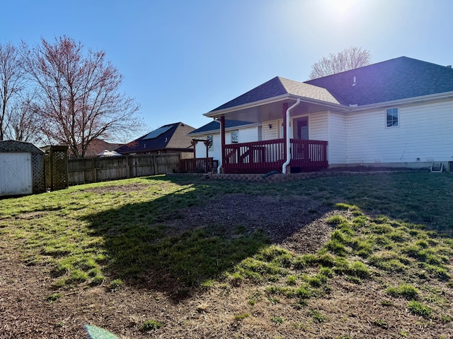 back of property featuring fence, roof with shingles, an outdoor structure, a storage shed, and a lawn