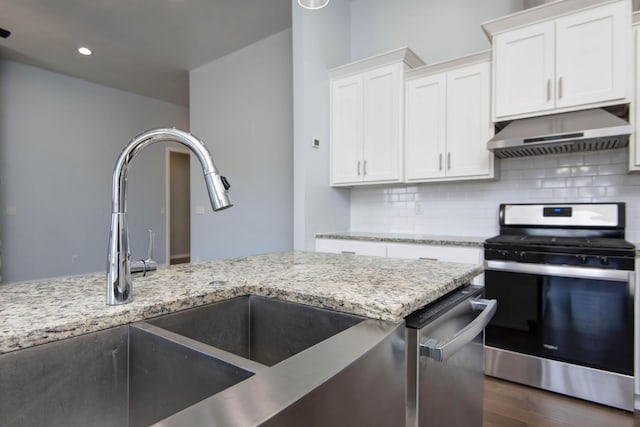 kitchen with under cabinet range hood, stainless steel appliances, tasteful backsplash, and white cabinetry