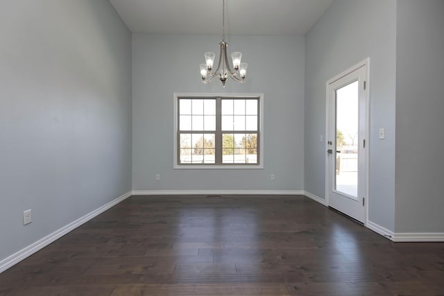 spare room with a chandelier, dark wood-type flooring, and baseboards