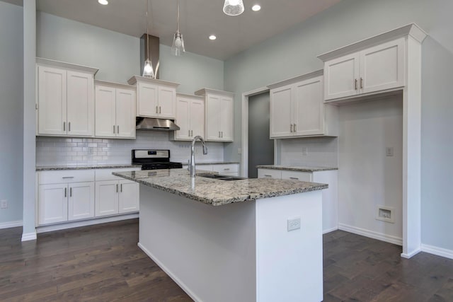 kitchen with under cabinet range hood, gas stove, white cabinetry, and a kitchen island with sink