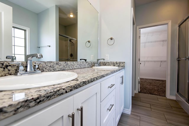 bathroom featuring double vanity, a shower stall, a walk in closet, and a sink