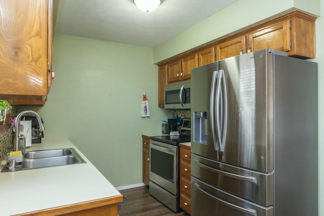 kitchen featuring brown cabinetry, dark wood finished floors, a sink, light countertops, and appliances with stainless steel finishes