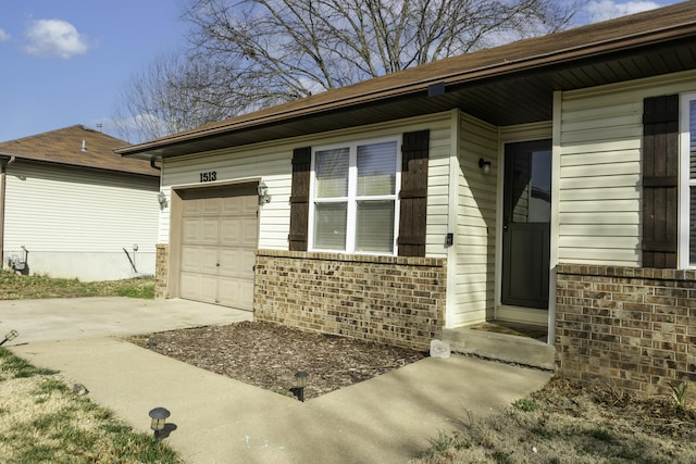 doorway to property featuring an attached garage, brick siding, and driveway