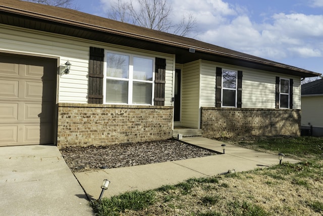 doorway to property with an attached garage, brick siding, and driveway