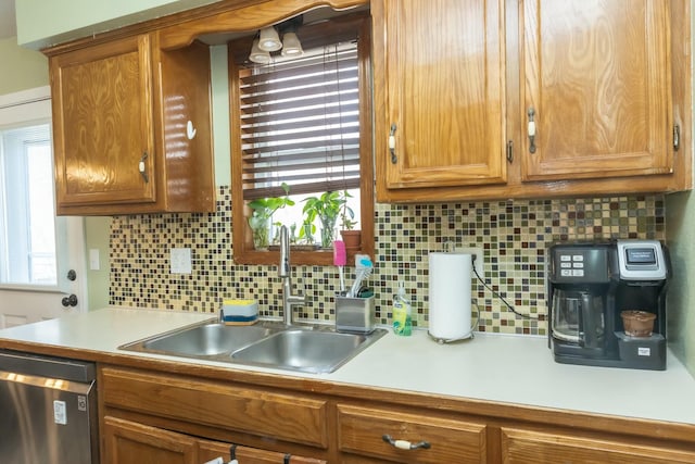 kitchen with brown cabinets, a sink, light countertops, stainless steel dishwasher, and tasteful backsplash